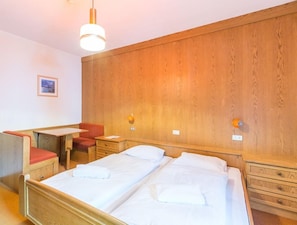 A hotel room with two beds, a desk, a chair, and wooden paneling on the walls. - Chalet Hotel Diamant (San Martino in Badia)