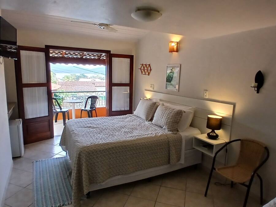 Un dormitorio con cama, mesita de noche, lámpara, silla y un balcón con sillas.