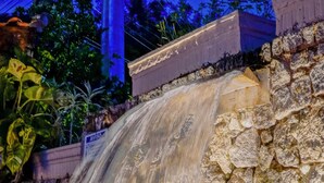 A waterfall feature with a stone wall backdrop and a pool below. - Pousada do Forte (Paraty)