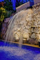 Una cascada con un muro de piedra de fondo y una piscina debajo.
