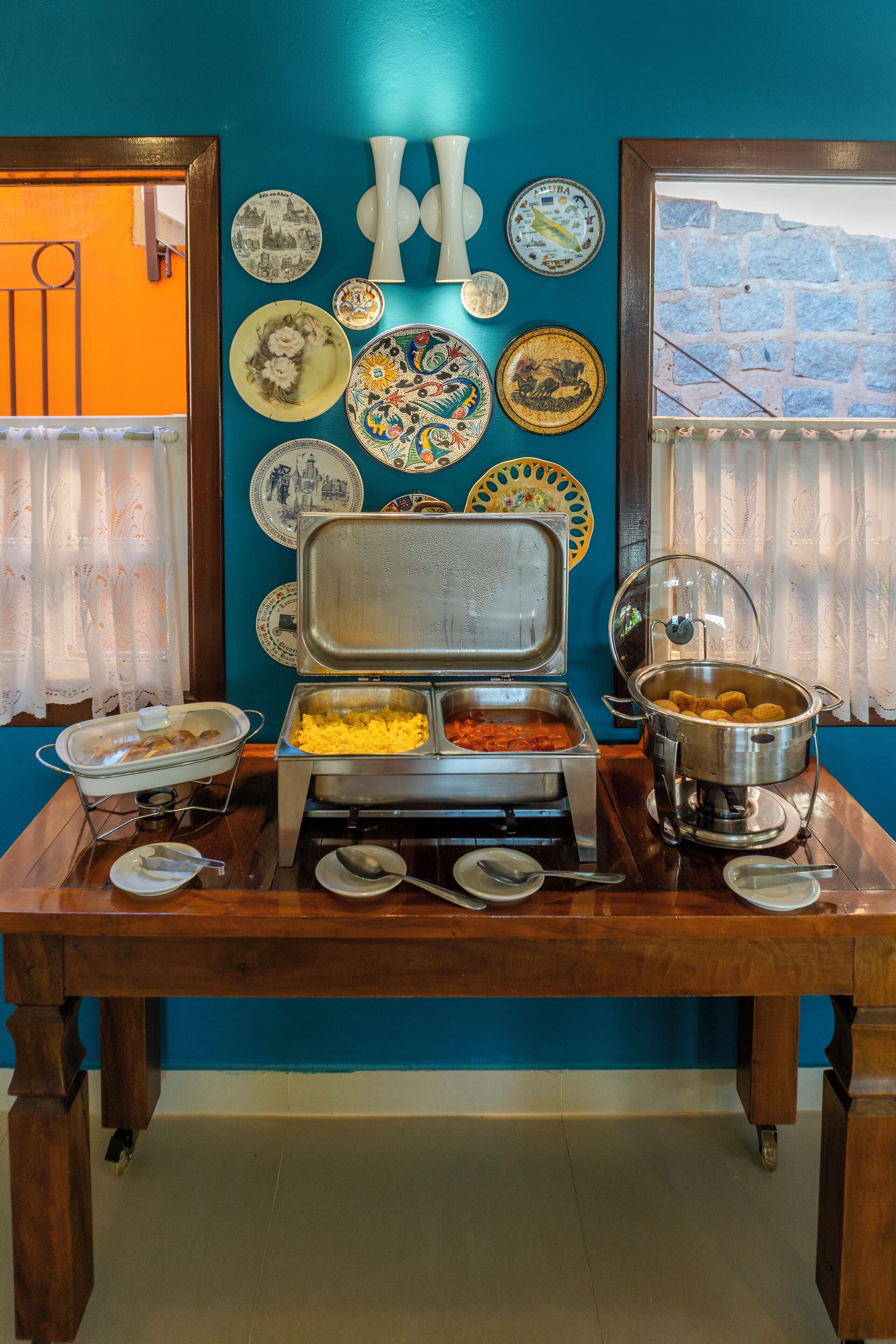 Un tavolo per buffet con diversi piatti, una parete decorata con piatti e una finestra vista su un muro di pietra.