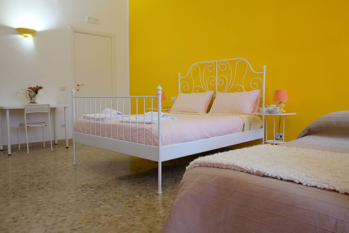 Un dormitorio con una estructura de cama metálica blanca, una pared amarilla y una puerta blanca.