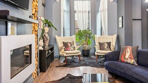 Un salon moderne avec une cheminée, deux fauteuils, un canapé et une grande plante.