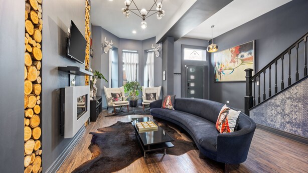 Un salon moderne avec un canapé bleu foncé, une table basse en verre et un mur décoré de rondins de bois.