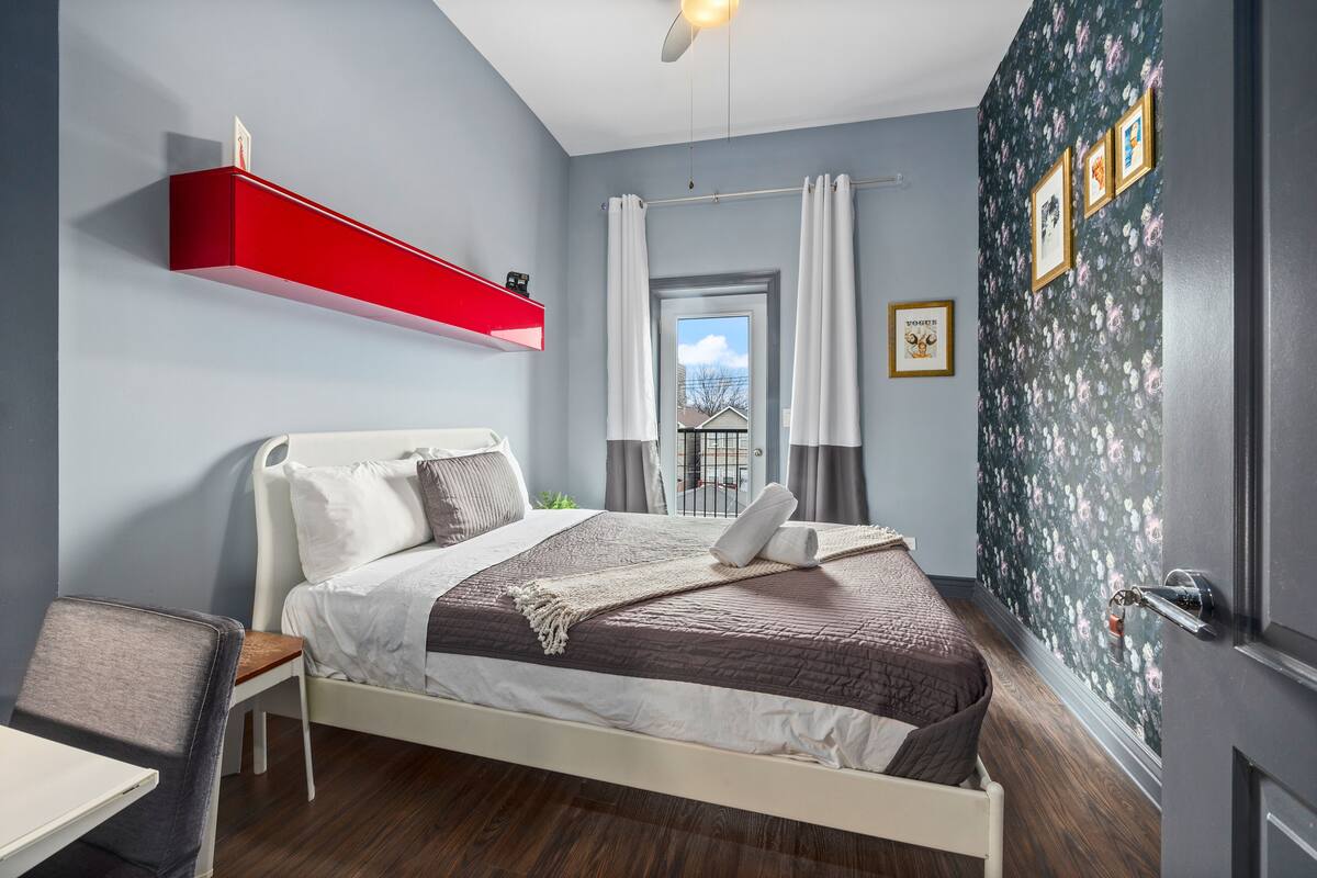 Una camera da letto con un letto, una scrivania, una sedia, uno scaffale rosso e una finestra con tende.