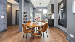 Un espace repas moderne avec une table et des chaises en bois, un lustre et une vue sur la cuisine.