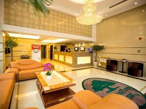 Un vestíbulo de hotel con una recepción, sofás, una máquina de café y una alfombra decorativa.