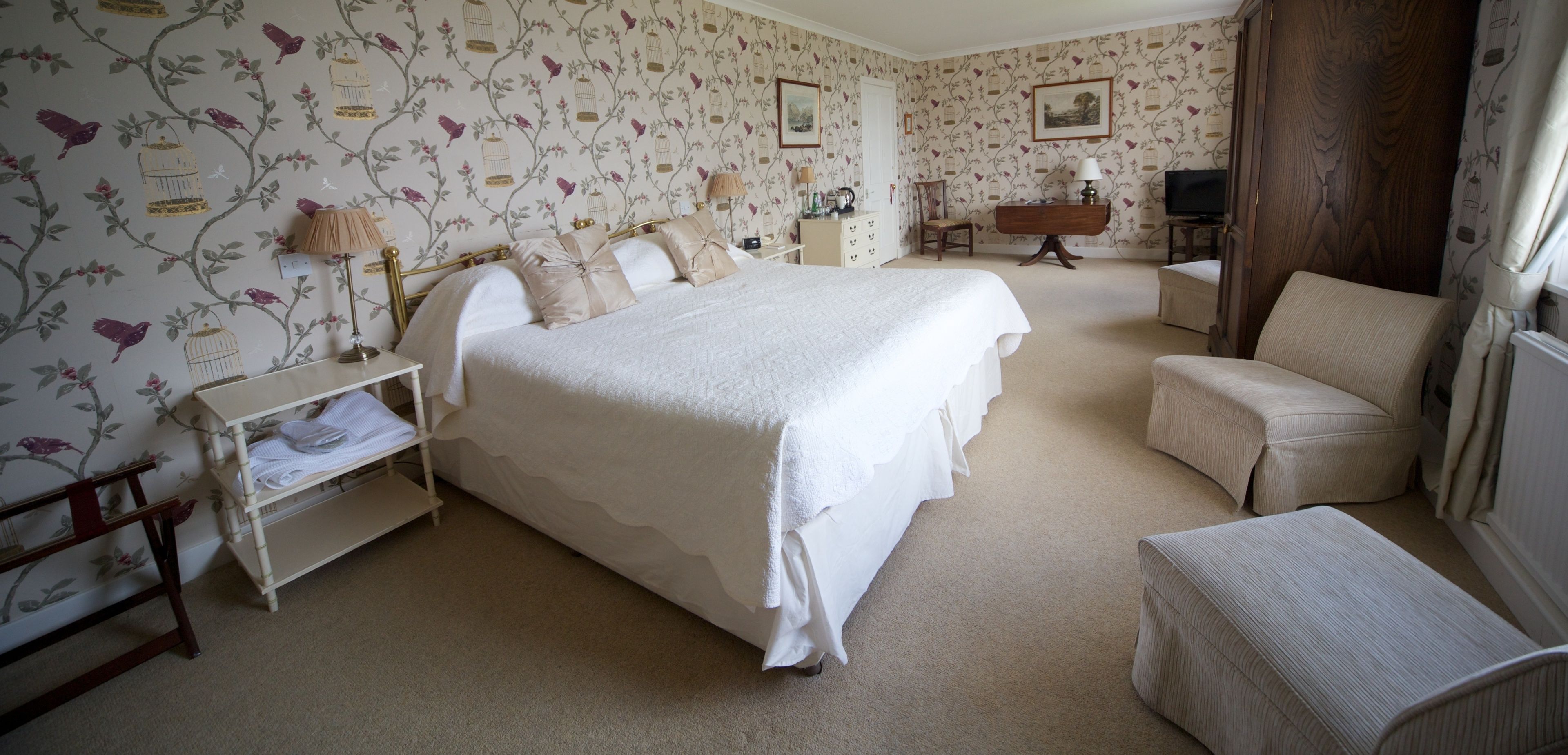 A bedroom with a large bed, a bedside table, a chair, a dresser, and a television.