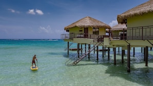 Waterbungalows met rieten daken, helder turquoise water en iemand die op een paddleboard staat.