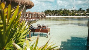 An overwater bungalows with clear water, palm trees, and a beach in the background. - Palafitos Overwater Bungalows, All & More Inclusive - Adults Only - All inclusive (Playa del Carmen)