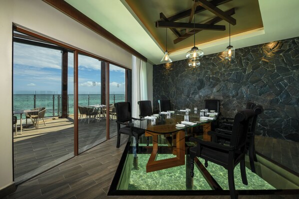 A dining area with a glass table, chairs, and a view of the ocean.