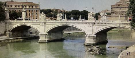 A stone bridge with multiple arches over a river, surrounded by buildings and trees.