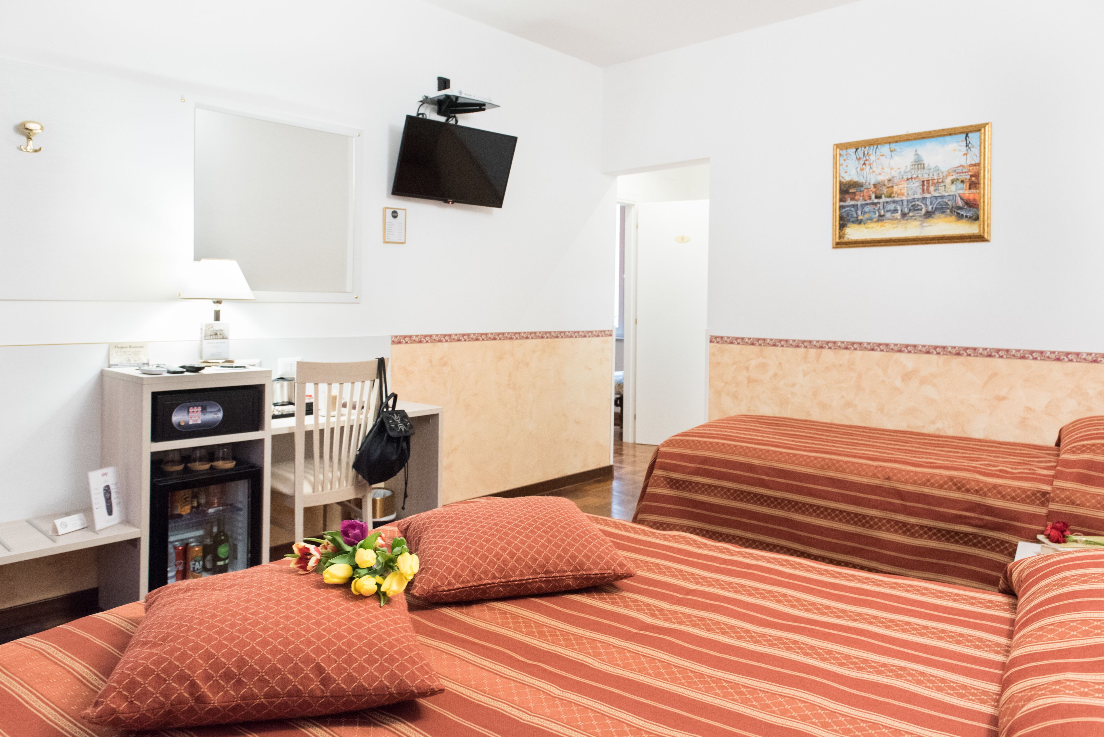 A hotel room with two beds, a TV, a painting, a minibar, and a desk with a lamp.