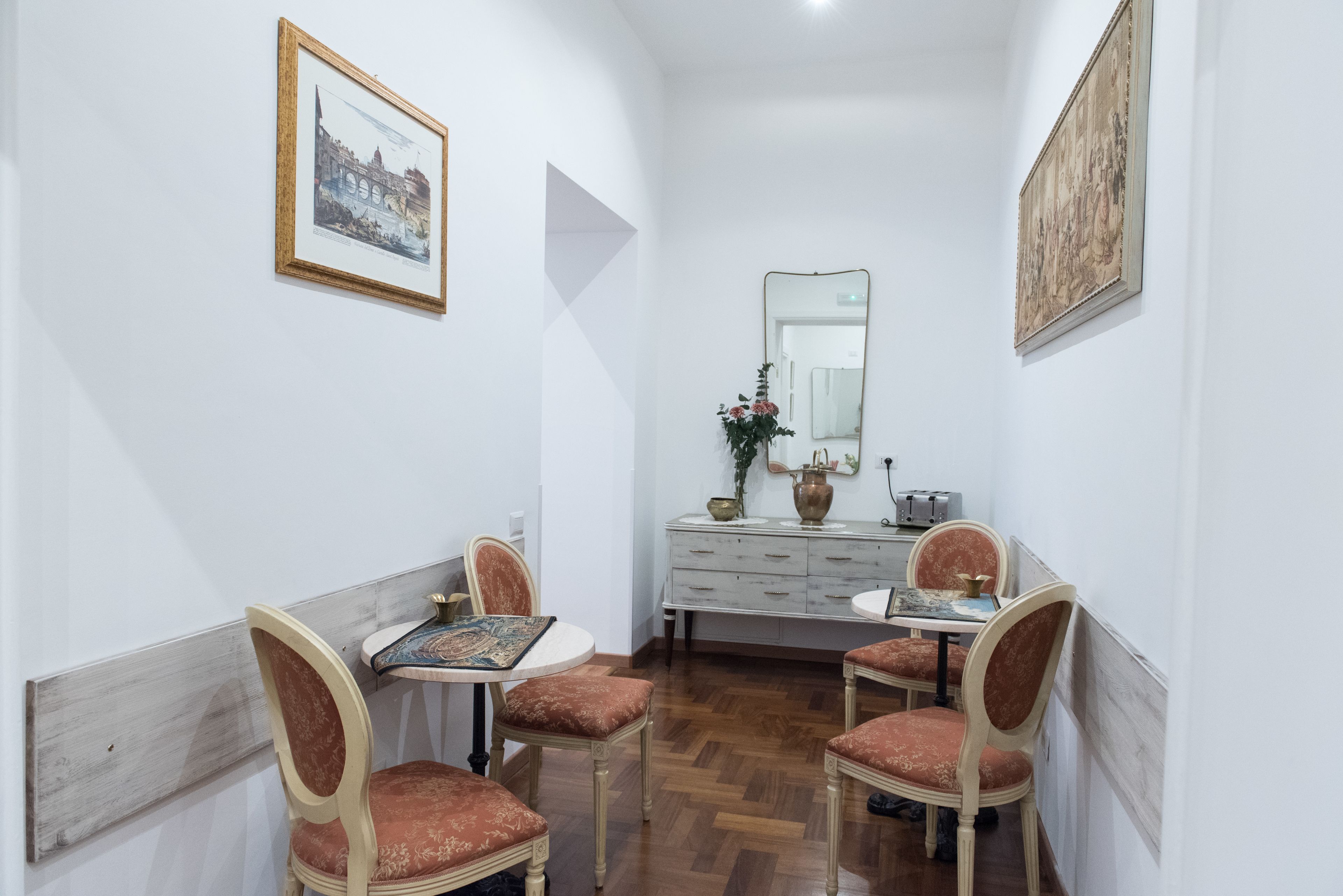 A dining area with a wooden table, four chairs, a white cabinet, and two framed pictures on the walls.