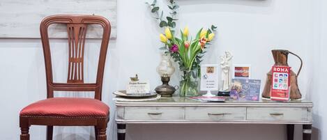 A wooden chair with a red cushion, a white desk with a vase of flowers, a statue, and a poster.