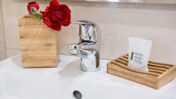 Een wastafel met een houten doosje met daarin een rode roos, een moderne kraan en een zeepdispenser.