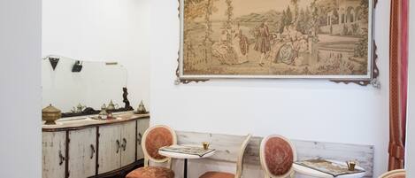 A dining area with a vintage-style table and chairs, a large framed landscape painting, and a wooden cabinet with decorative items.