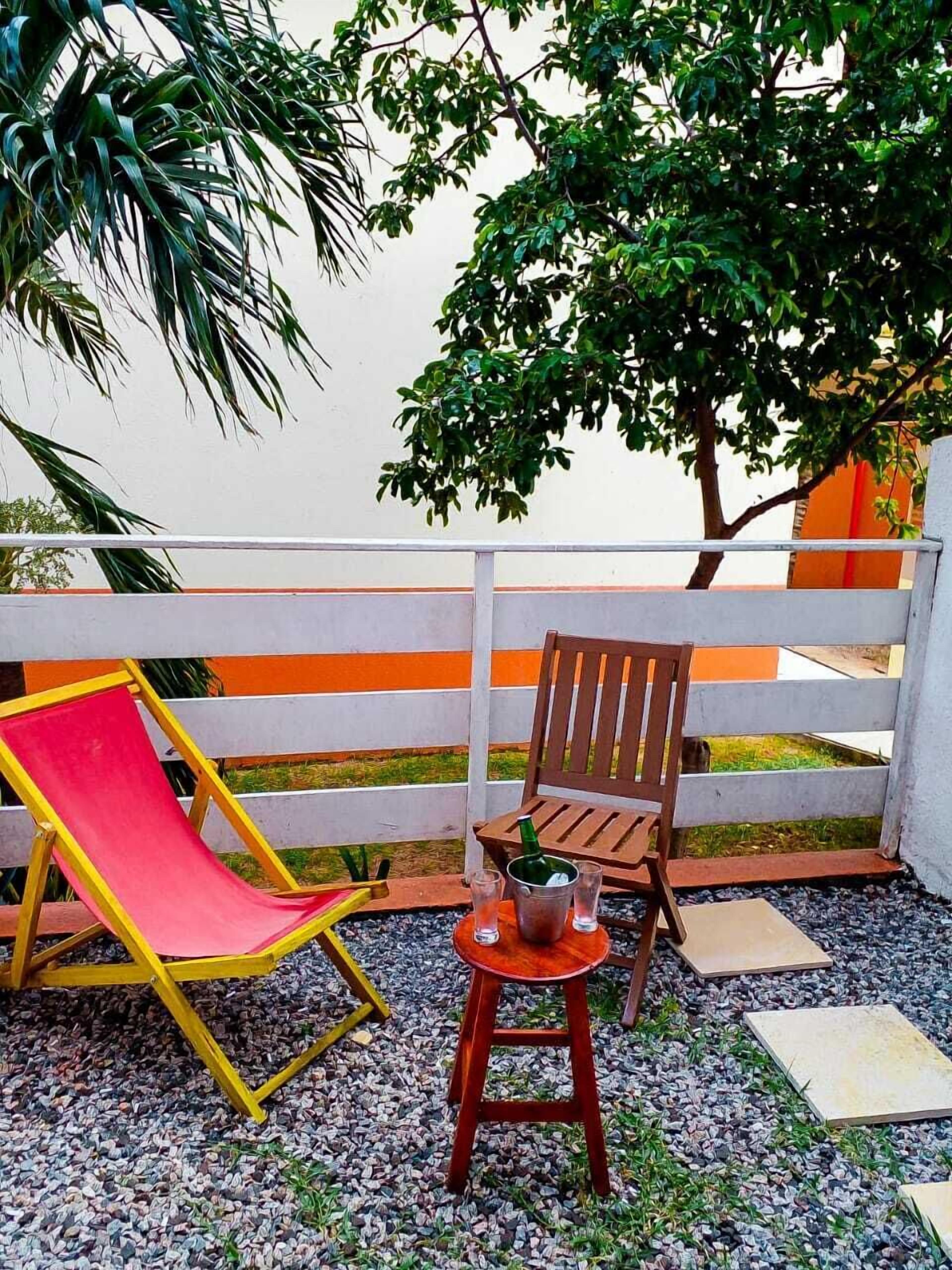 Eine Terrasse mit einem roten Liegestuhl, einem Holzstuhl und einem kleinen Tisch mit einer Flasche und Schnapsgläsern.