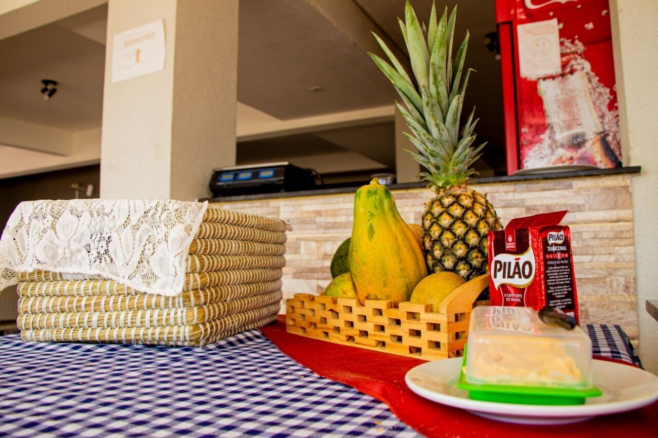 Uma área de cozinha com uma mesa coberta por um tecido xadrez, uma cesta de vime, uma abacaxi, um abóbora, uma embalagem de leite e um prato com uma fatia de queijo.