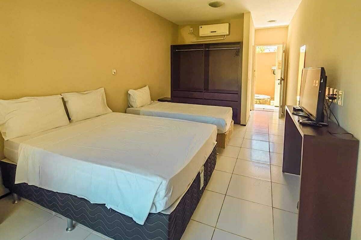 A hotel room with two beds, a wardrobe, a television, and a tiled floor.