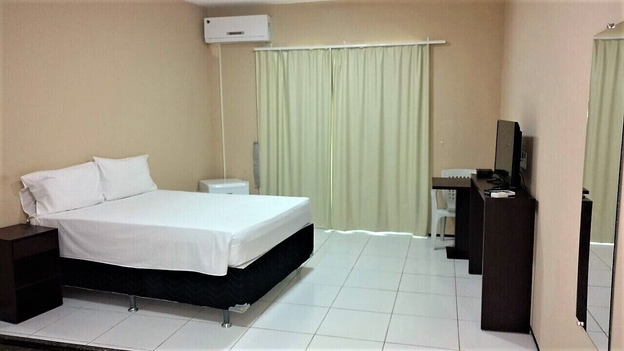 A hotel room with a bed, a desk, a chair, a TV, and a window with curtains.