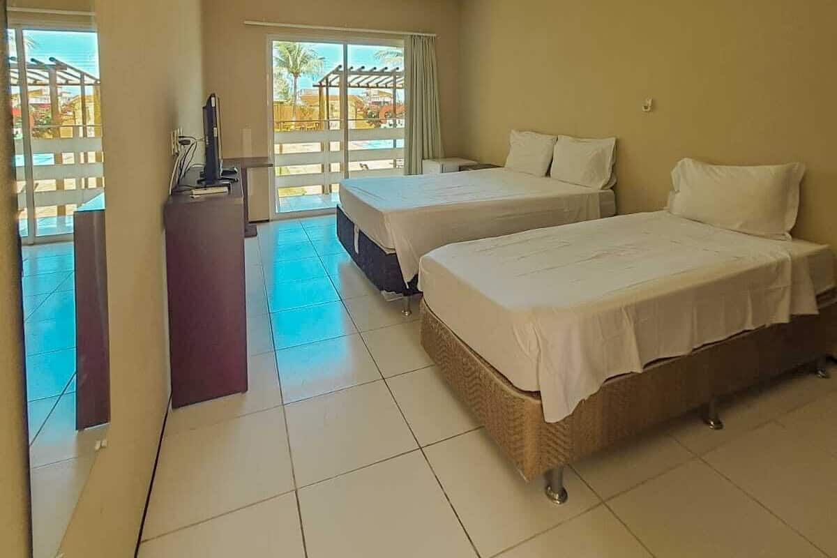 A hotel room with two beds, a desk with a computer, and a balcony with a view.
