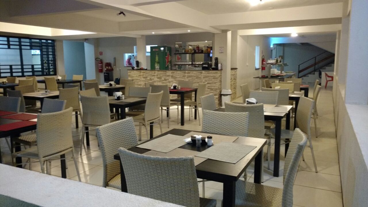 Um restaurante com várias mesas e cadeiras, uma área de bar e uma escadaria que leva a um andar superior.