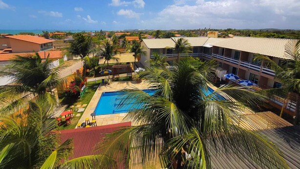A resort with a swimming pool, palm trees, and a view of the sea. - Hotel Dama Business Center (São Gonçalo do Amarante)