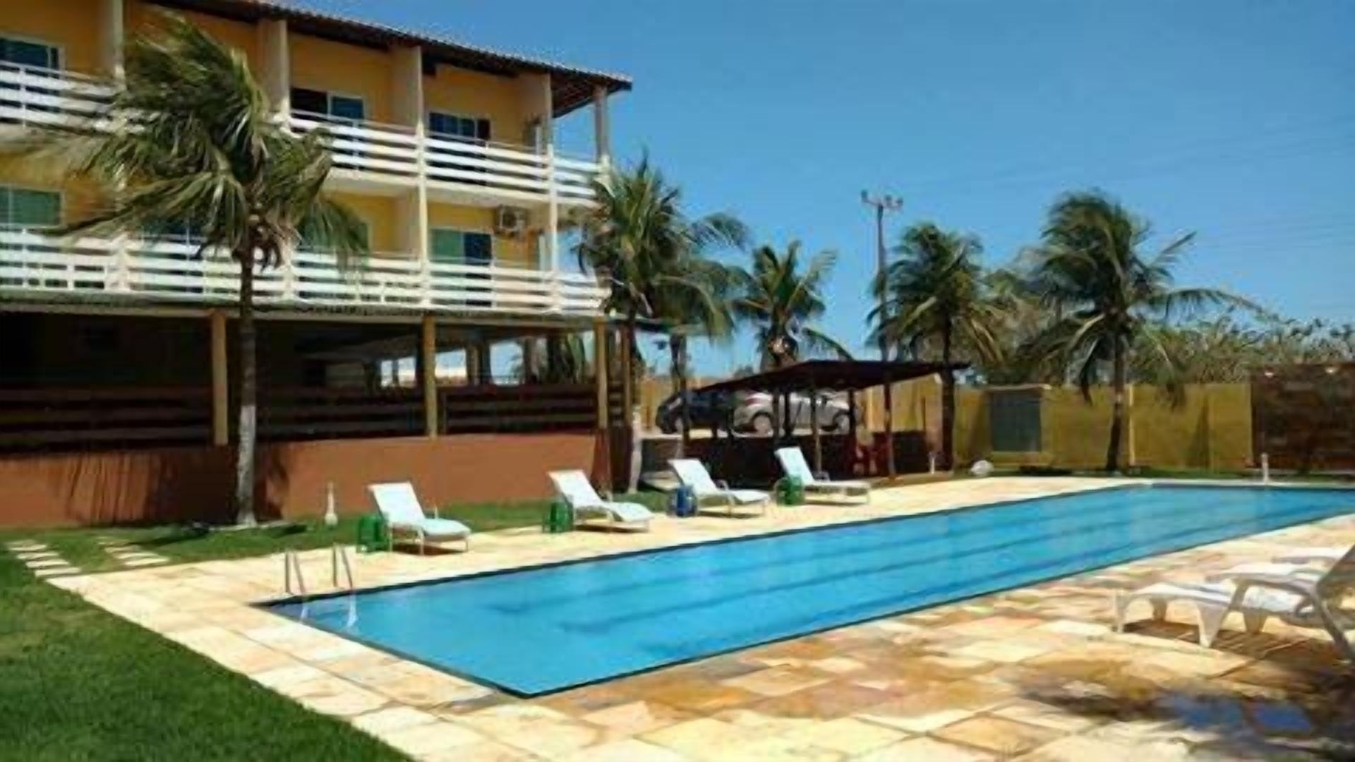 Una piscina con sillas de descanso, un área techada y palmeras.