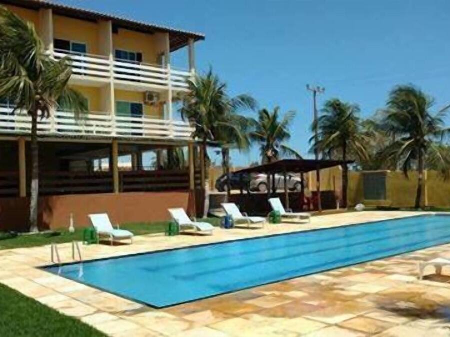 Una piscina con sillas de descanso, un área techada y palmeras.