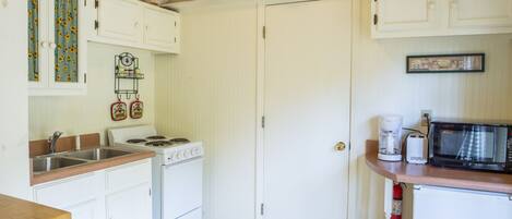 A kitchen with white cabinets, a stove, a microwave, and a sink.