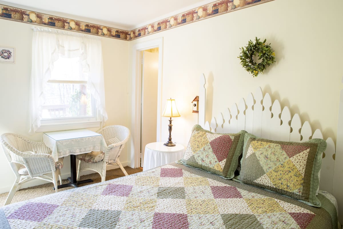 A cozy bedroom with a bed, a small table, two chairs, and a lamp.