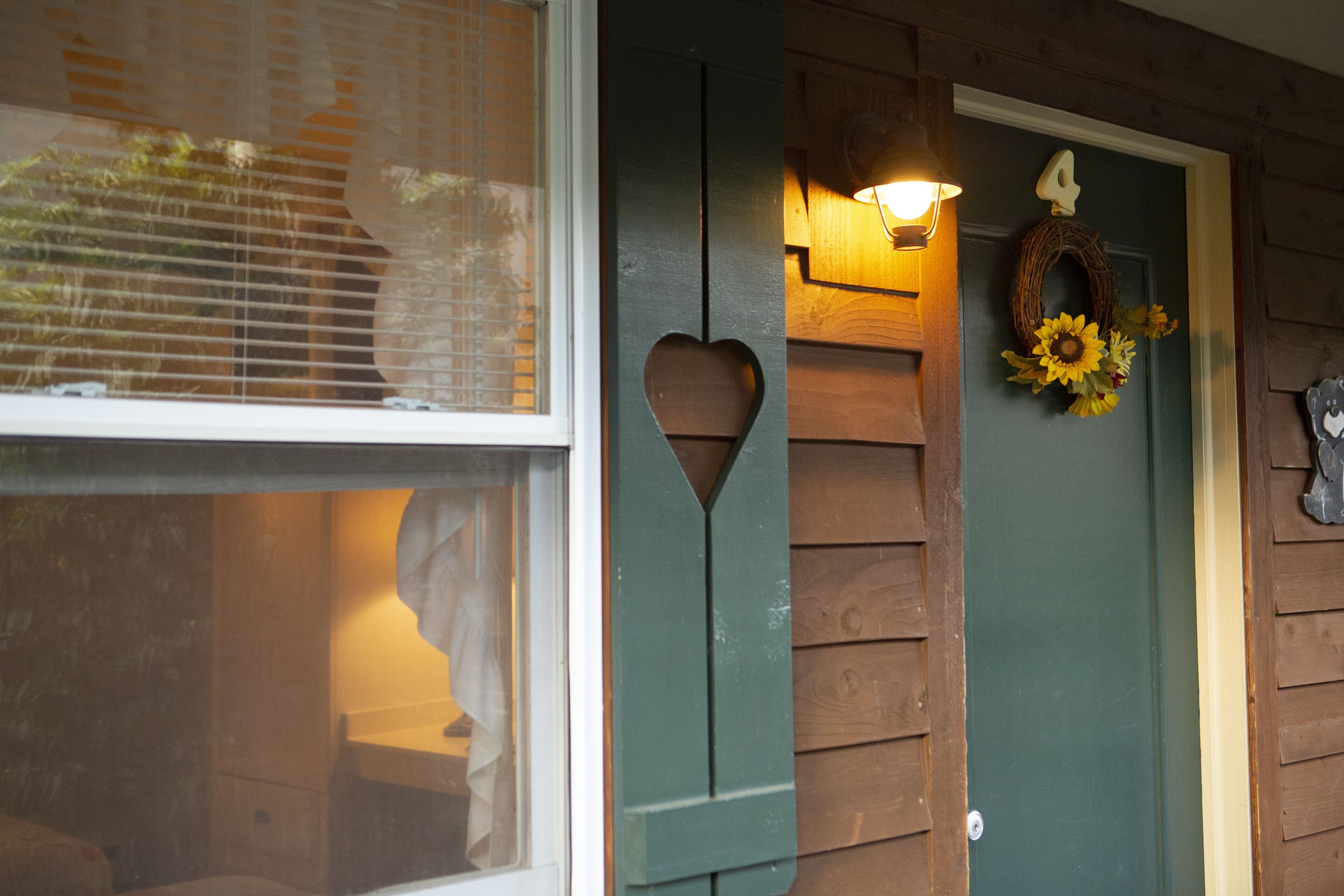 Une porte en bois ornée d’une découpe en forme de cœur, d’une plaque portant le chiffre « 4 » et d’une décoration représentant un tournesol.