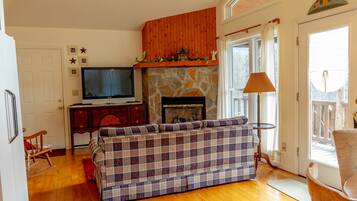 A living room with a stone fireplace, a plaid sofa, a television, and a wooden ceiling.