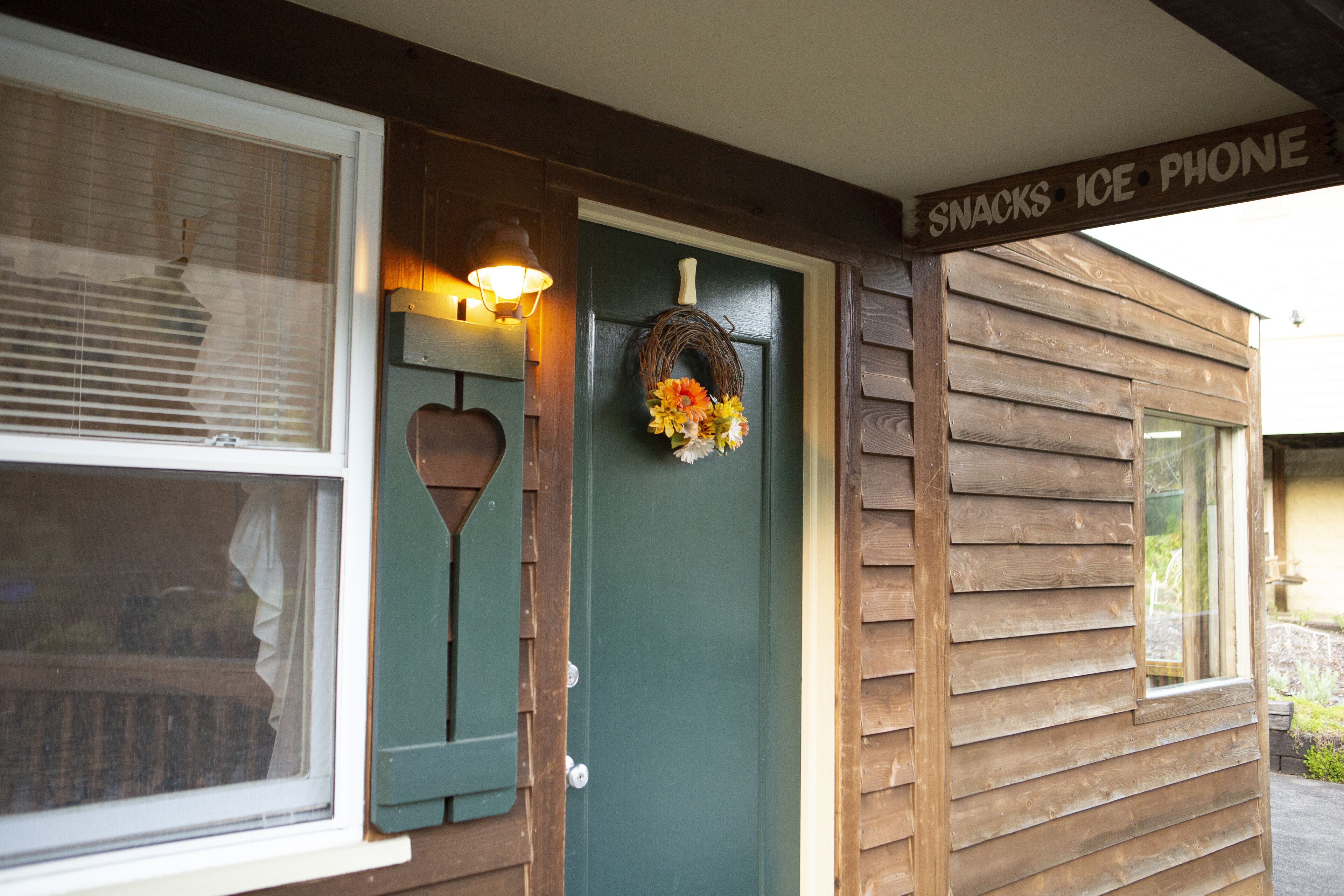A wooden building with a green door, a sign above the door reading "SNACKS ICE PHONE", and a wreath hanging on the door.
