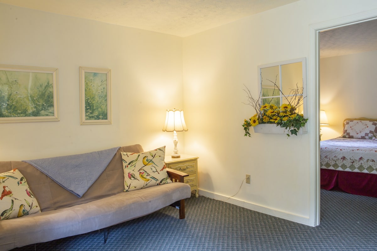 A cozy room with a sofa, a small table with a lamp, and a bed with a floral bedspread.