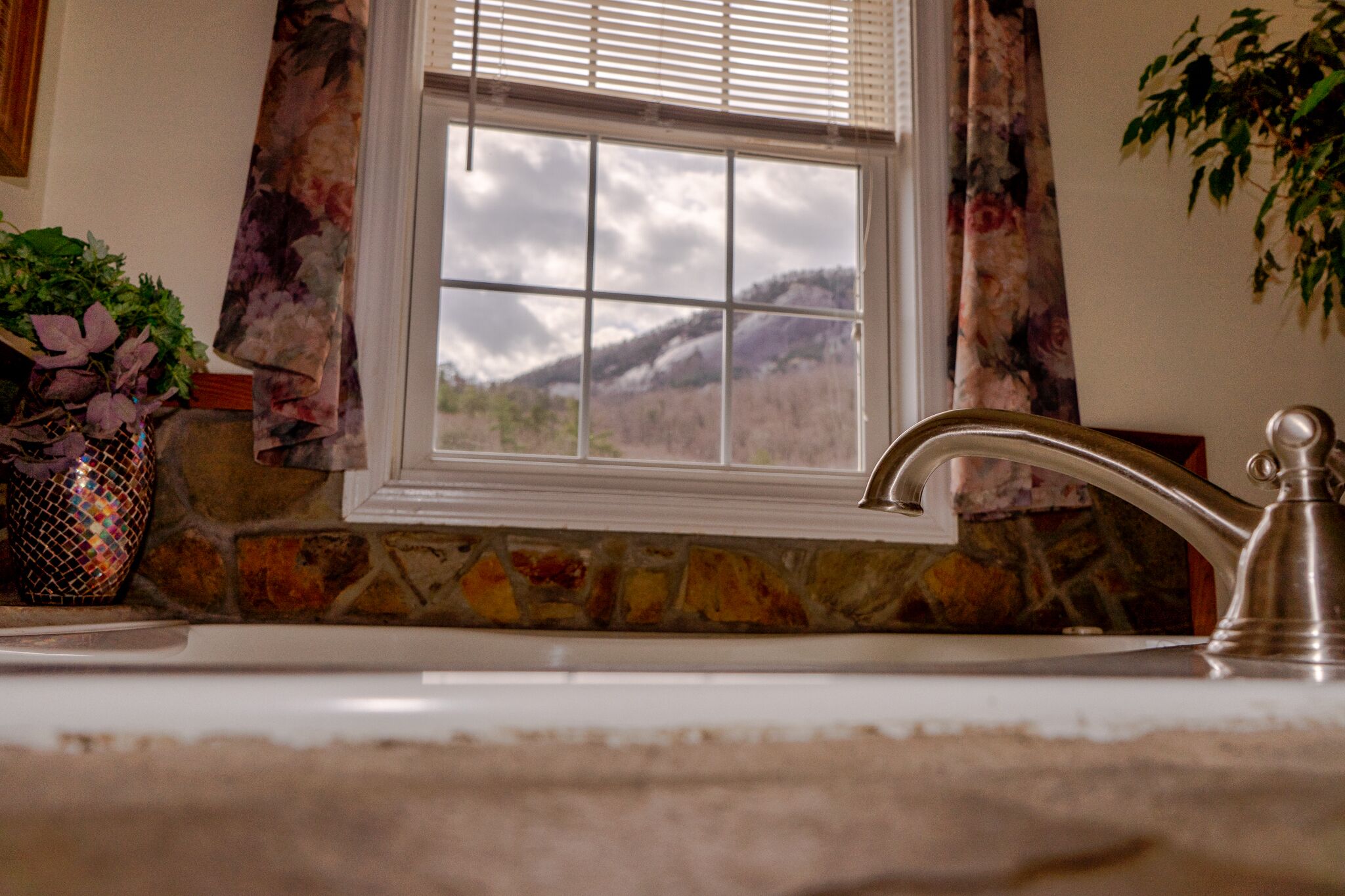 A bathroom with a stone wall, a window with a view of mountains, and a modern faucet.