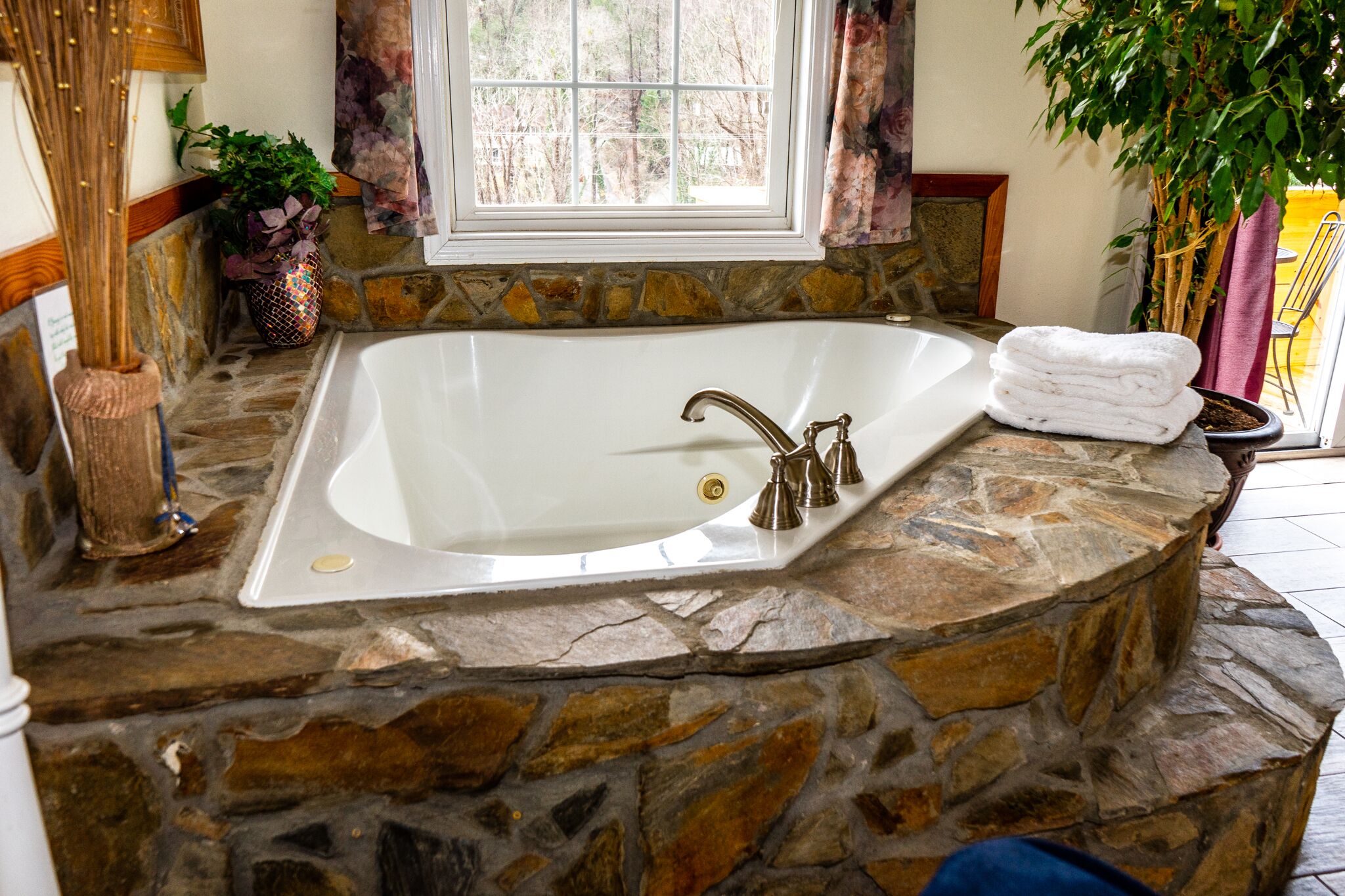 A stone-enclosed bathtub with a window above it, a potted plant, and a towel on the side.