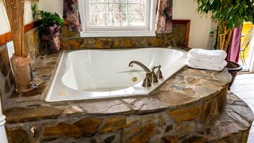 A stone-enclosed bathtub with a window above it, a potted plant, and a towel on the side.