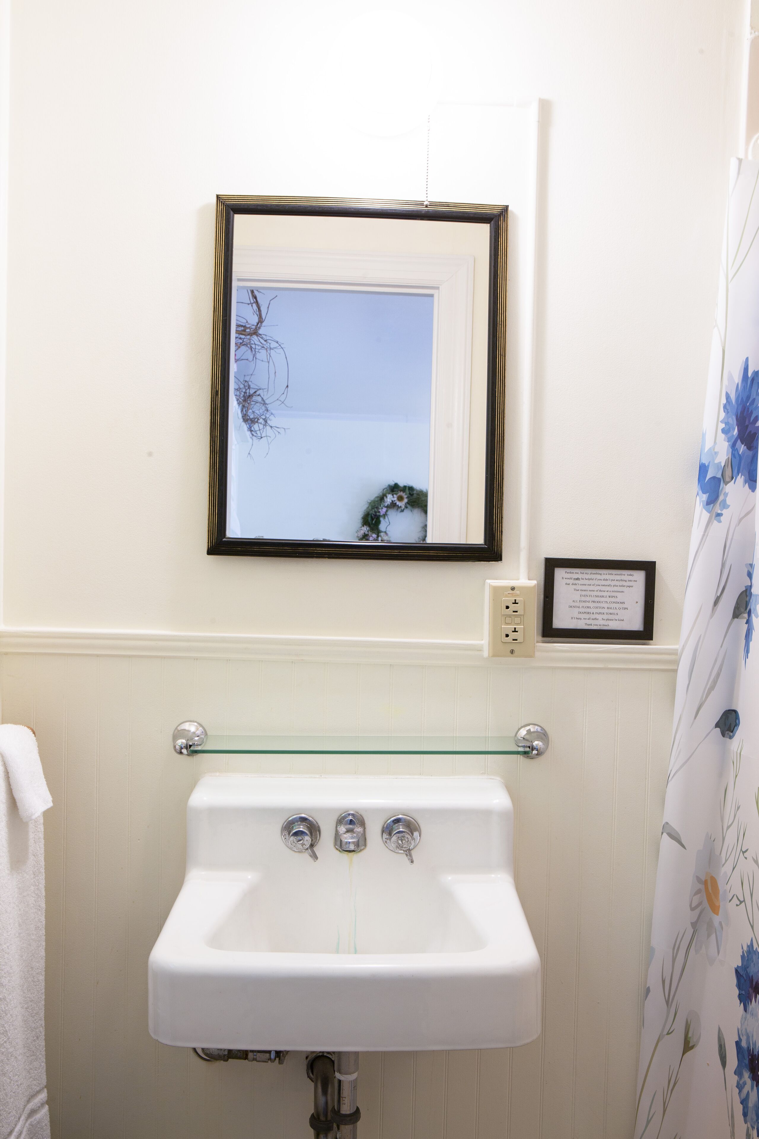 A bathroom with a white sink, a framed mirror, and a glass shelf above the sink.
