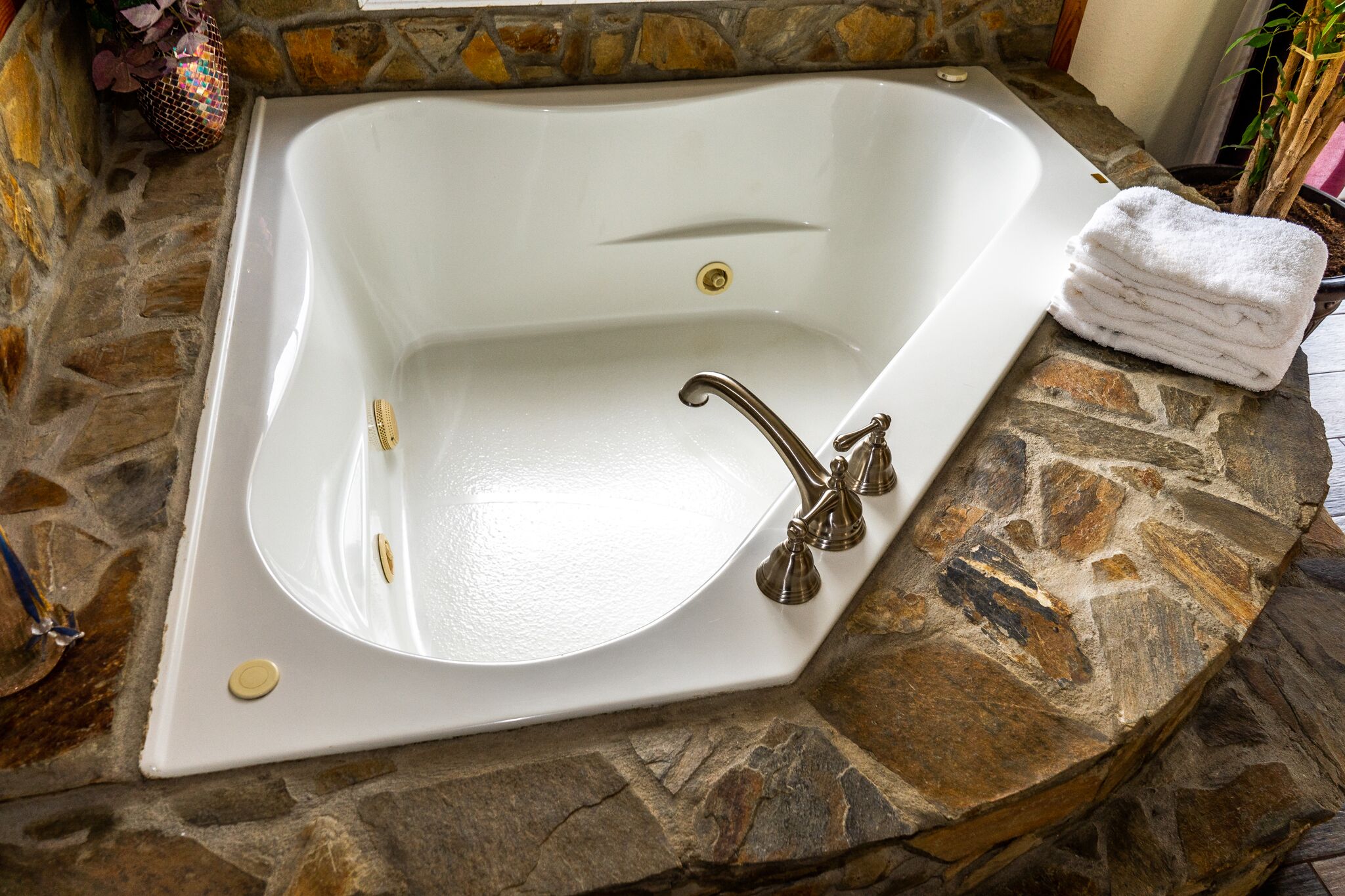 A white bathtub with a stone countertop, a gold faucet, and a stack of white towels.