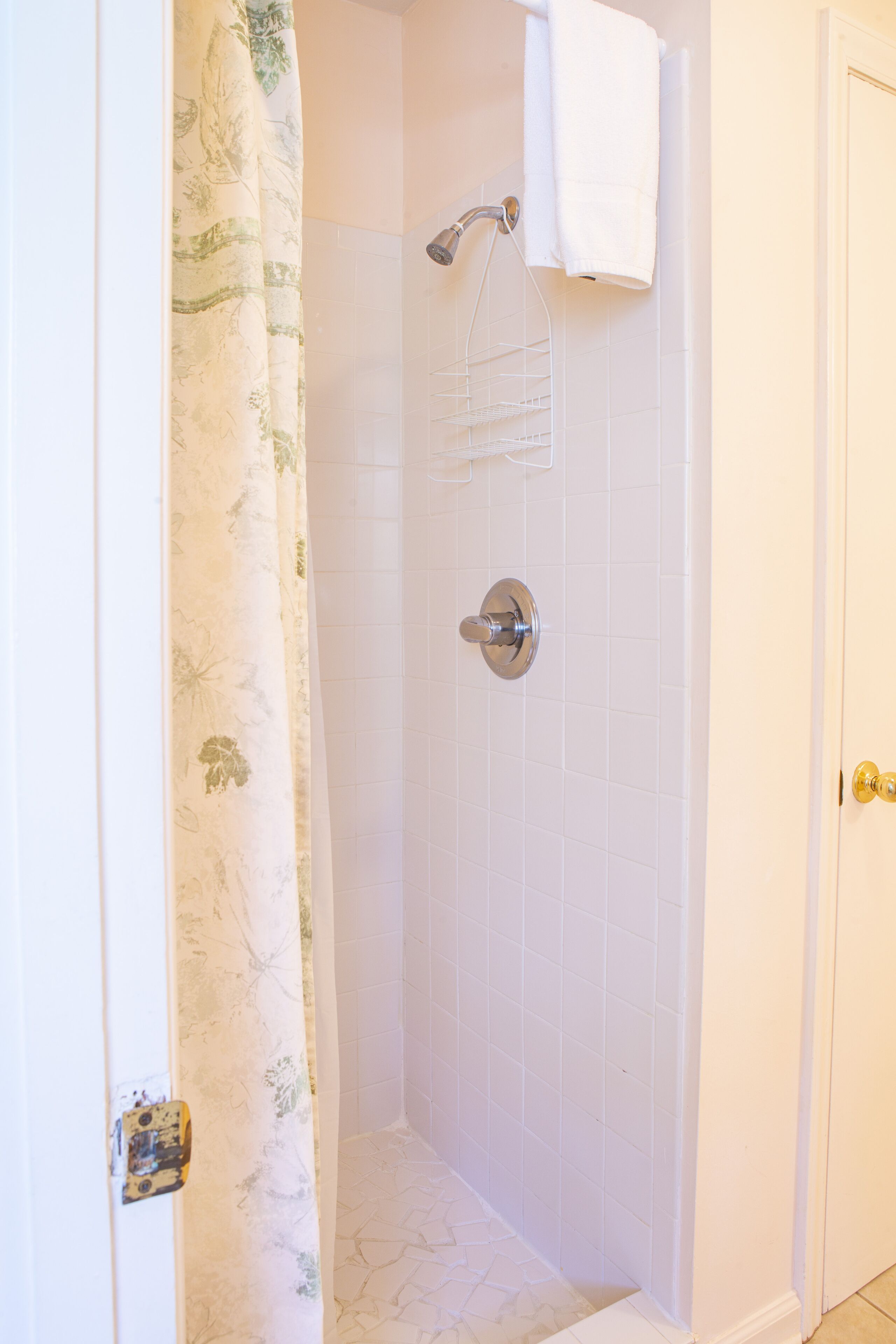 A bathroom with a shower, white tiled walls, a shower curtain, and a towel hanging on the wall.