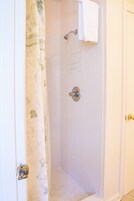 Un baño con ducha, paredes de azulejos blancos, cortina de ducha y una toalla colgada en la pared.