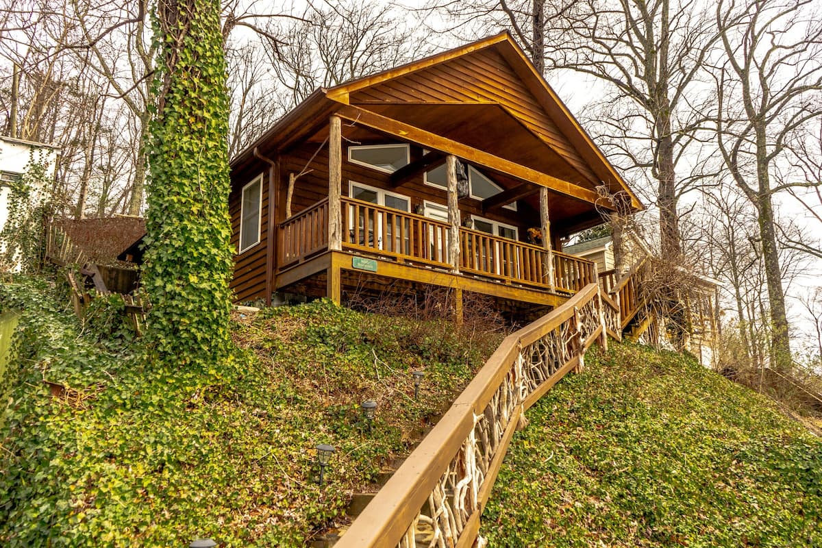 A wooden cabin with a balcony, surrounded by trees and greenery.