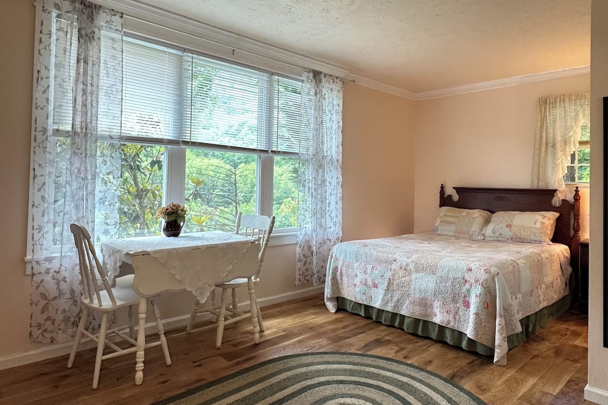 A bedroom with a wooden bed, a small table with chairs, and a window with curtains.