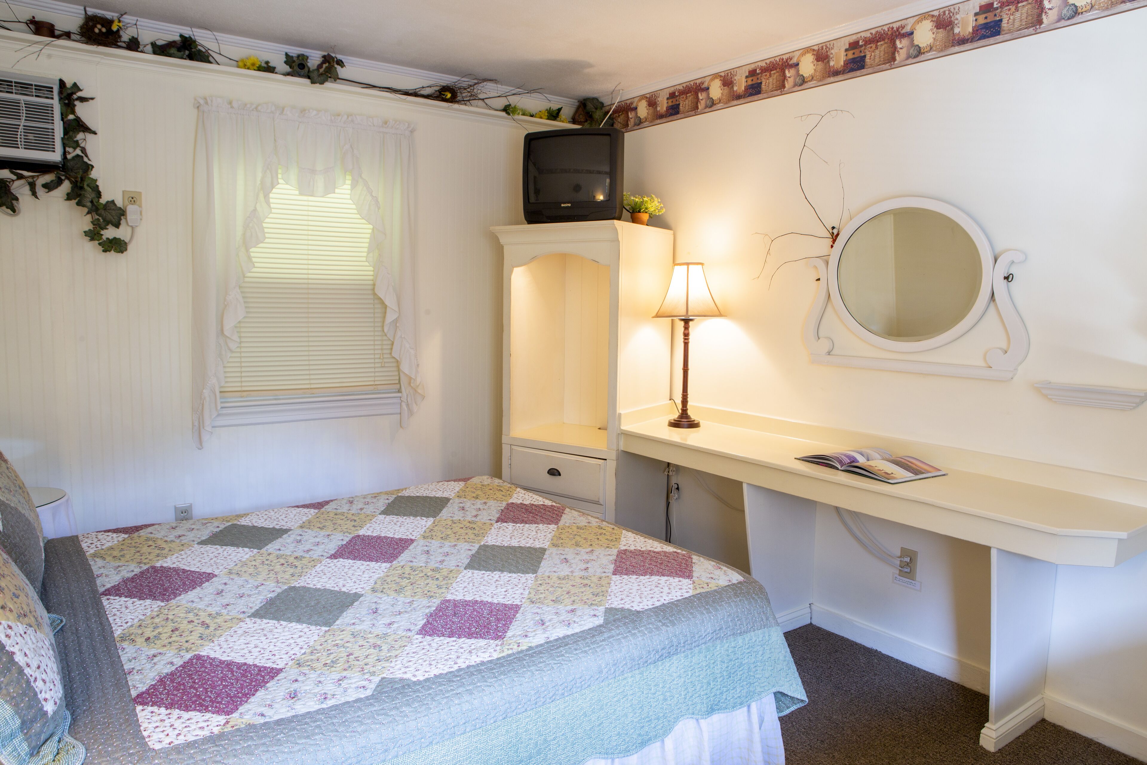 Une chambre à coucher avec un lit, une commode, un miroir et une fenêtre avec des stores.