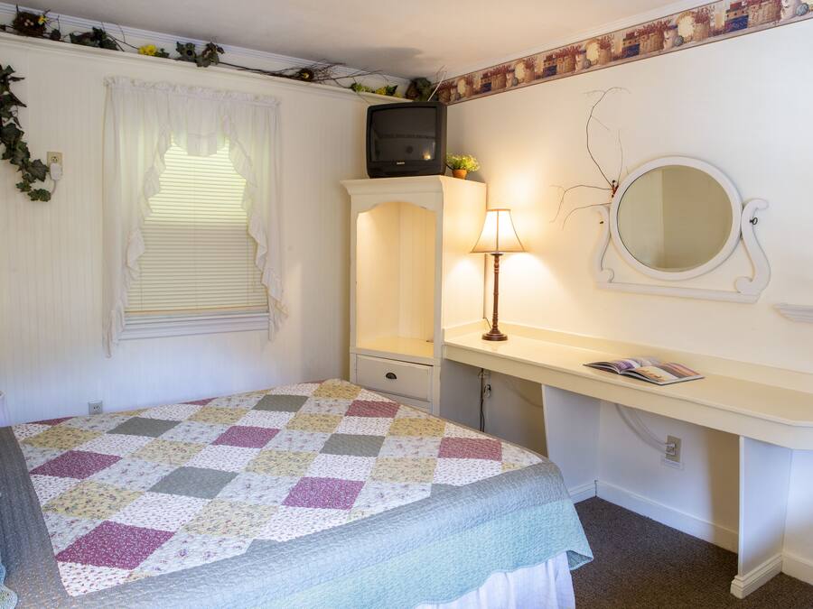 A bedroom with a bed, a dresser, a mirror, and a window with blinds.