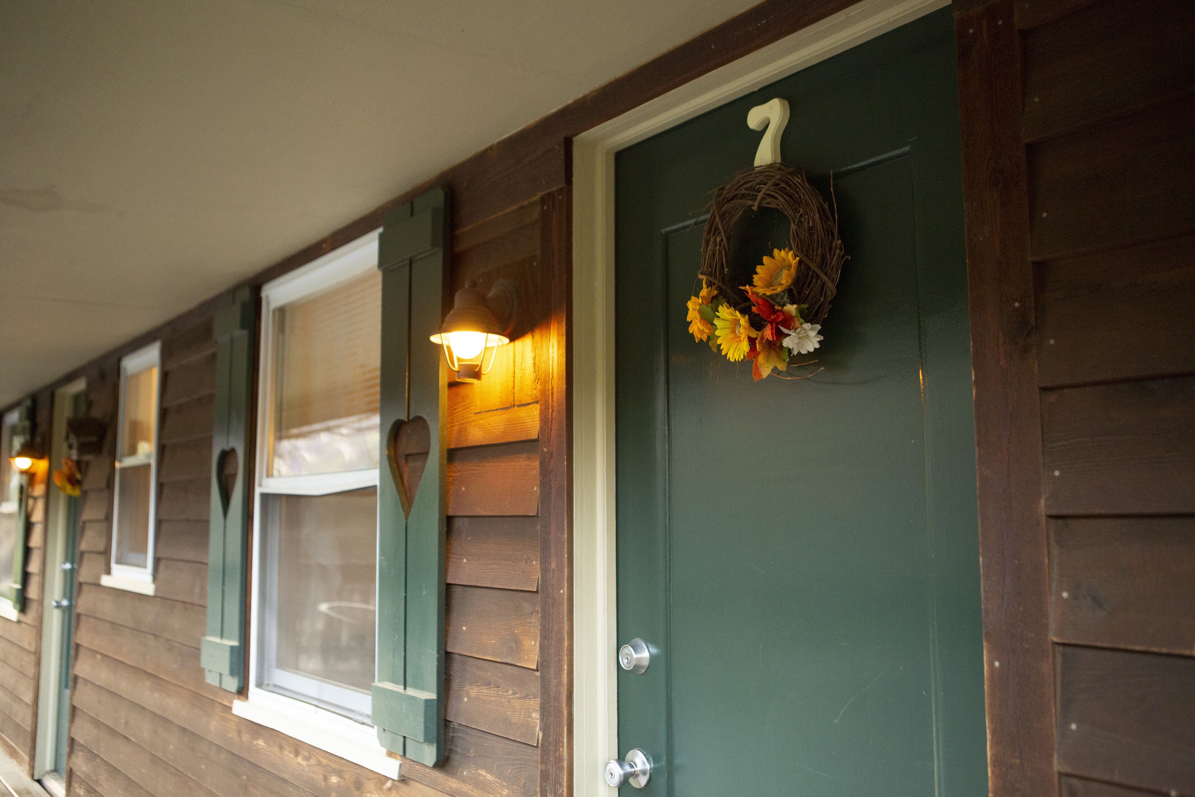 A row of wooden cabins with green doors, each featuring a wreath with flowers.