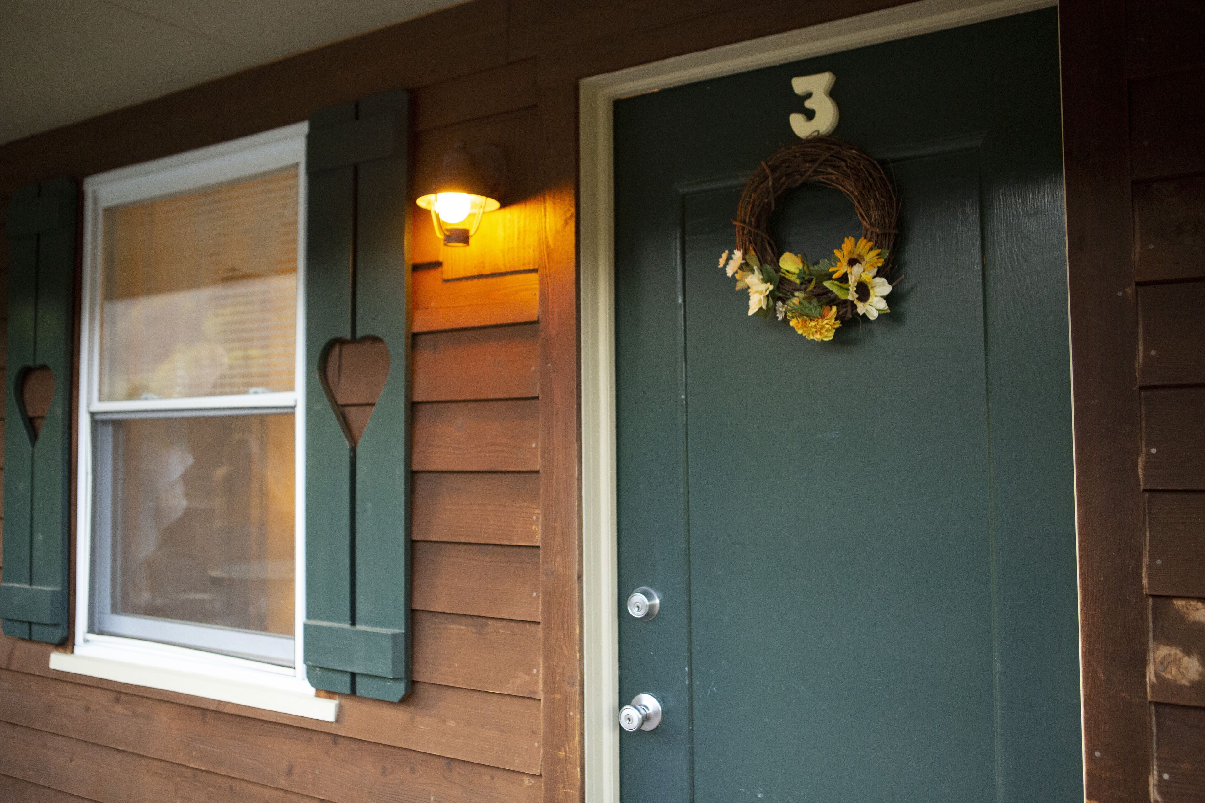 A house with a green door, a number '3' above the door, a wreath with flowers, and a window with shutters.