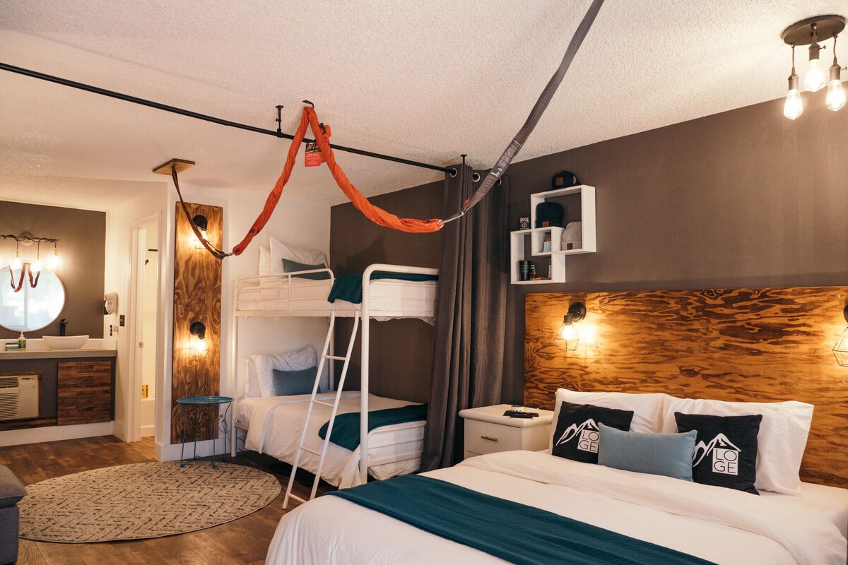 Une chambre d’hôtel moderne avec un lit superposé, une tête de lit en bois, une table de chevet et un grand miroir.